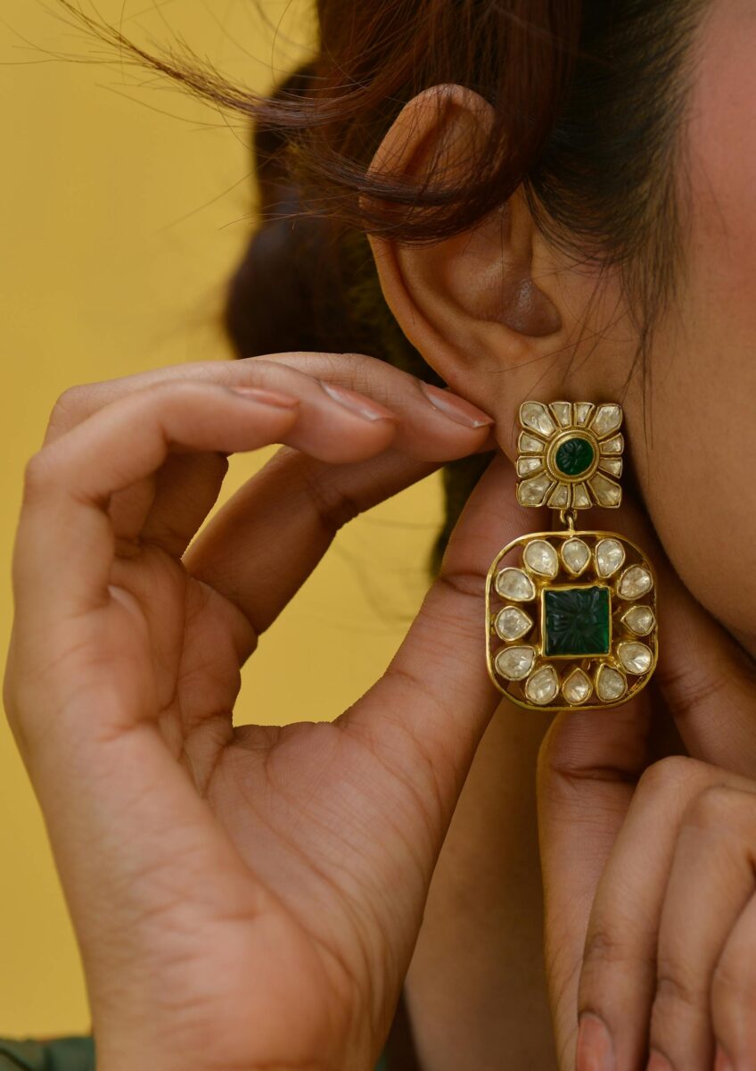Close-up of emerald and diamond earrings on a woman's ear.