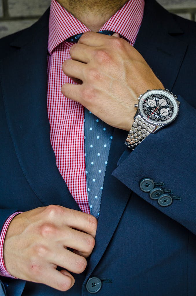 Stylish man adjusting tie, showcasing formal suit and luxury wristwatch.